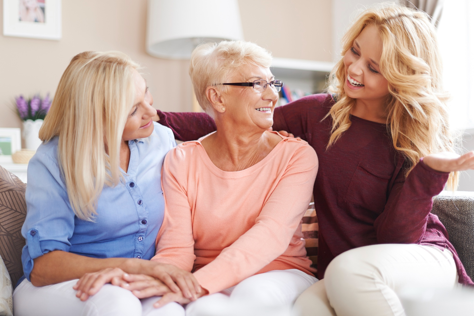 A senior resident sitting on a couch with her daughter and granddaughter.