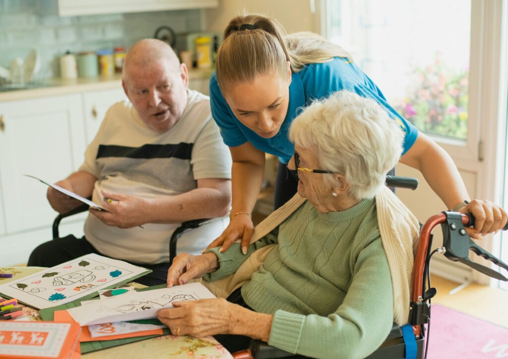 Two seniors sitting in wheelchairs while a caregiver checks in.