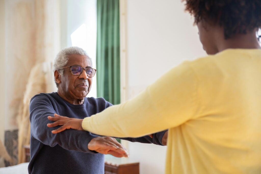A senior resident doing exercises with the help of a caregiver.
