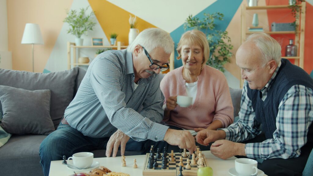 Three seniors sitting on a couch, drinking coffee, and playing a game of chess.