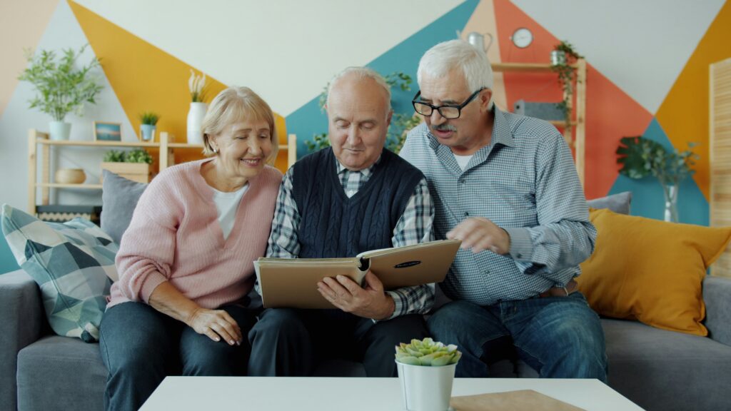 Three seniors sitting together on a couch, smiling while looking at a book.